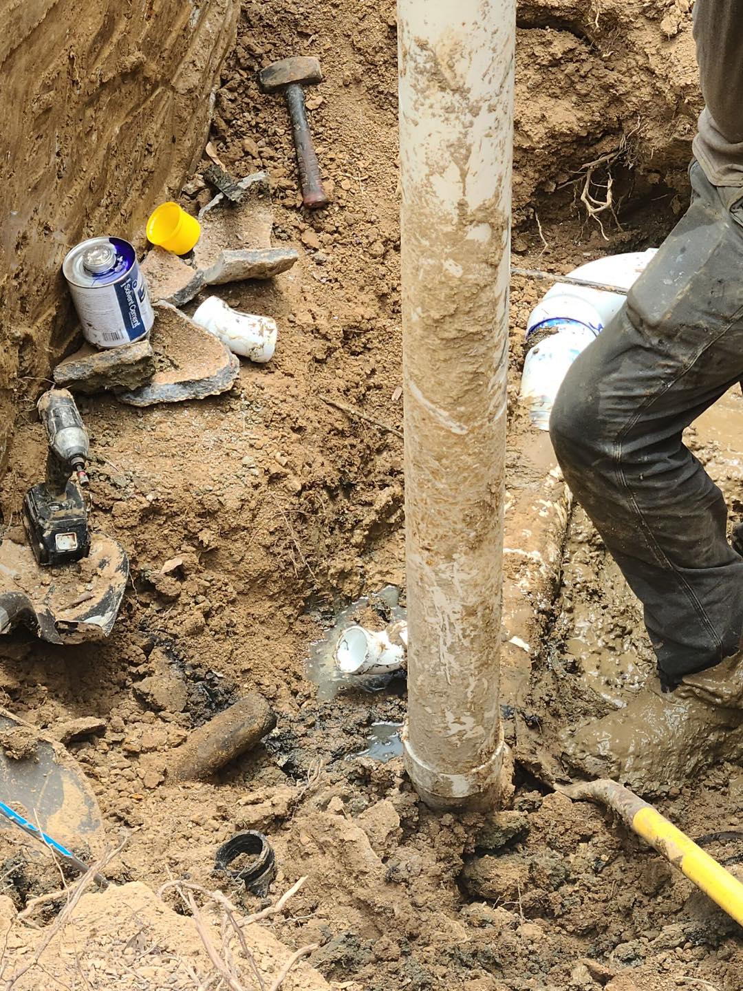 Plumber repairing a pipe down in a muddy trench